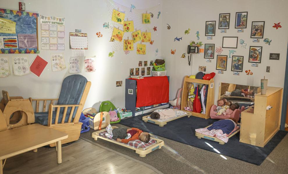 Toddlers sleep on mats on the floor in a childcare room decorated with toys and colorful wall decals