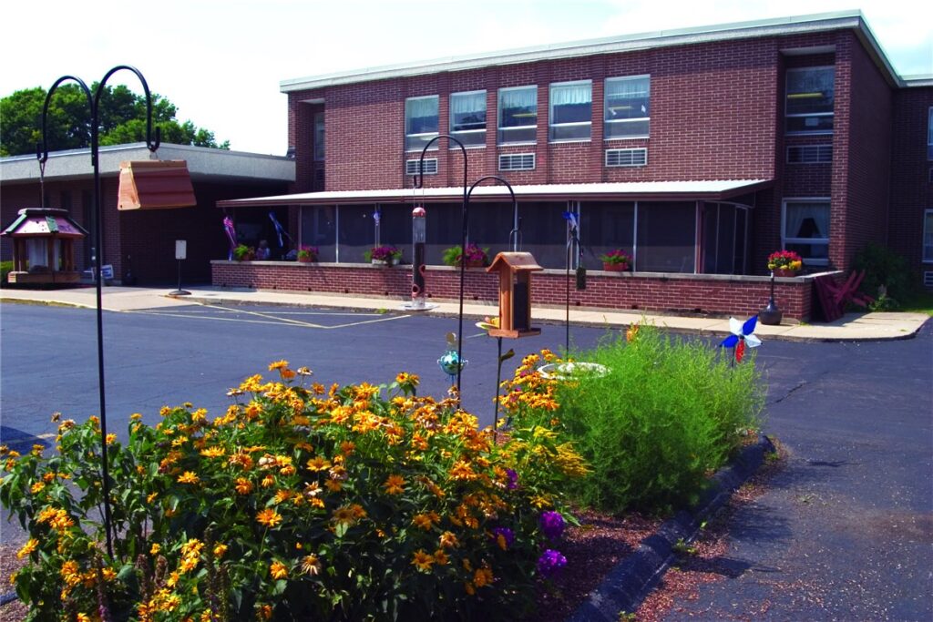A 2-story red brick building is shown with a parking lot and flowering landscaping shown in foreground.