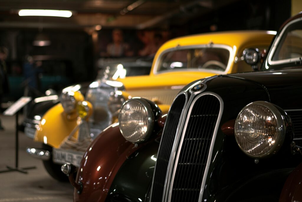 Two antique cars are shown. A maroon BMW is shown in the foreground and a yellow vehicle is show in the background.