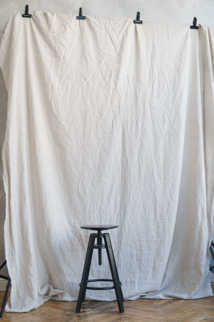 A white backdrop hangs from 4 clips behind a black stool with a swivel seat.